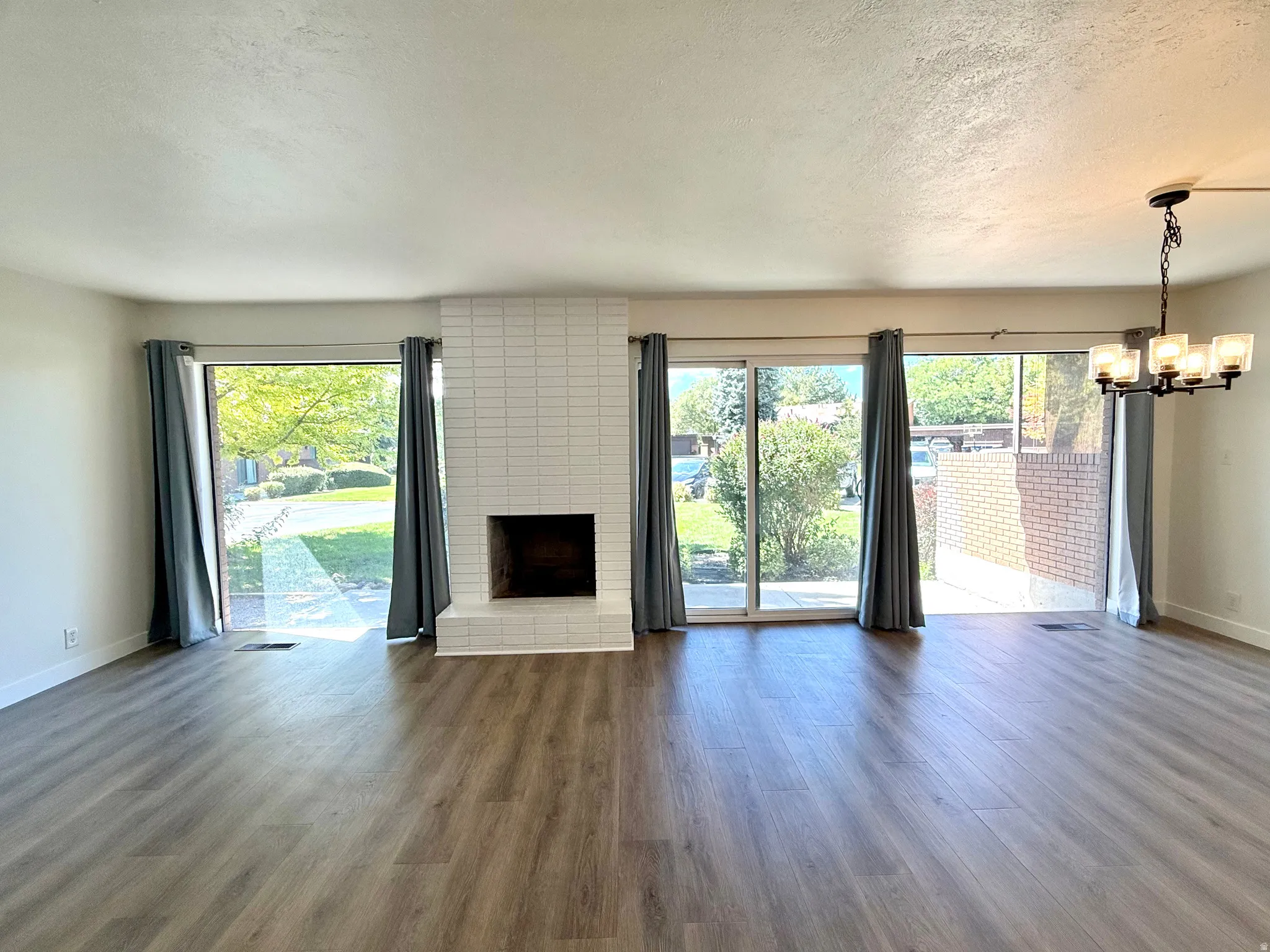 Wood-finish flooring, white brick fireplace, multiple sliding glass doors, and a multi-light chandelier