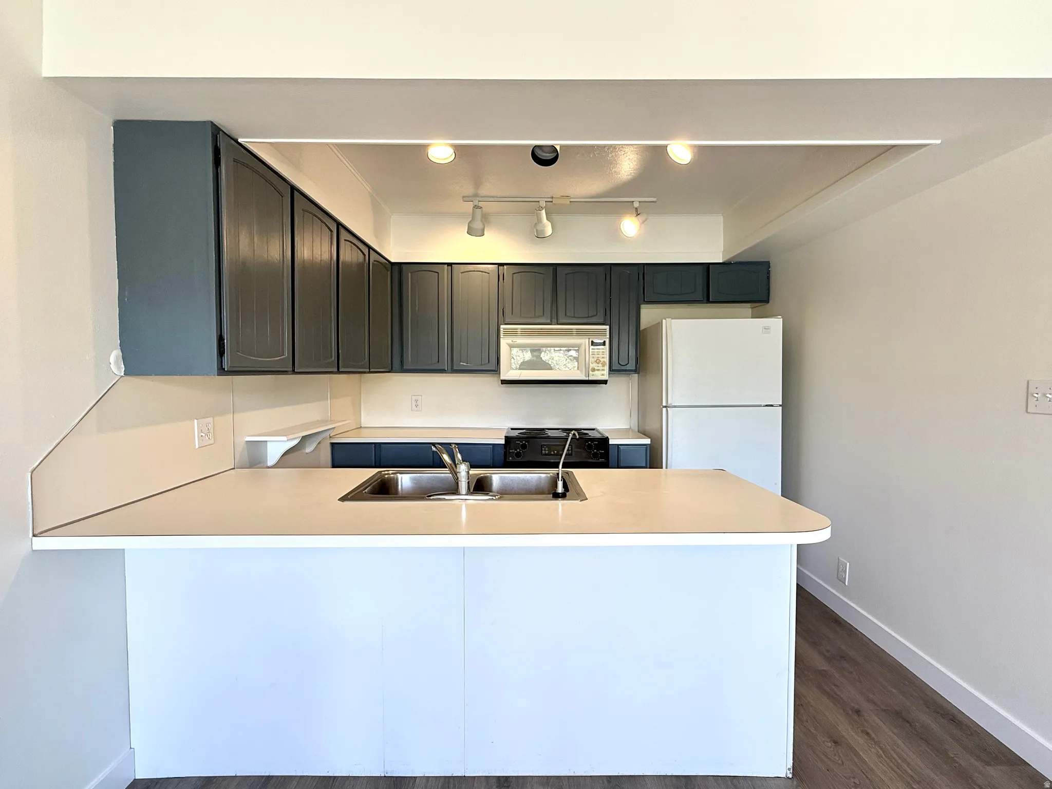 Kitchen featuring an integrated breakfast bar, blue cabinetry, stainless steel double basin sink, and wood-finish flooring