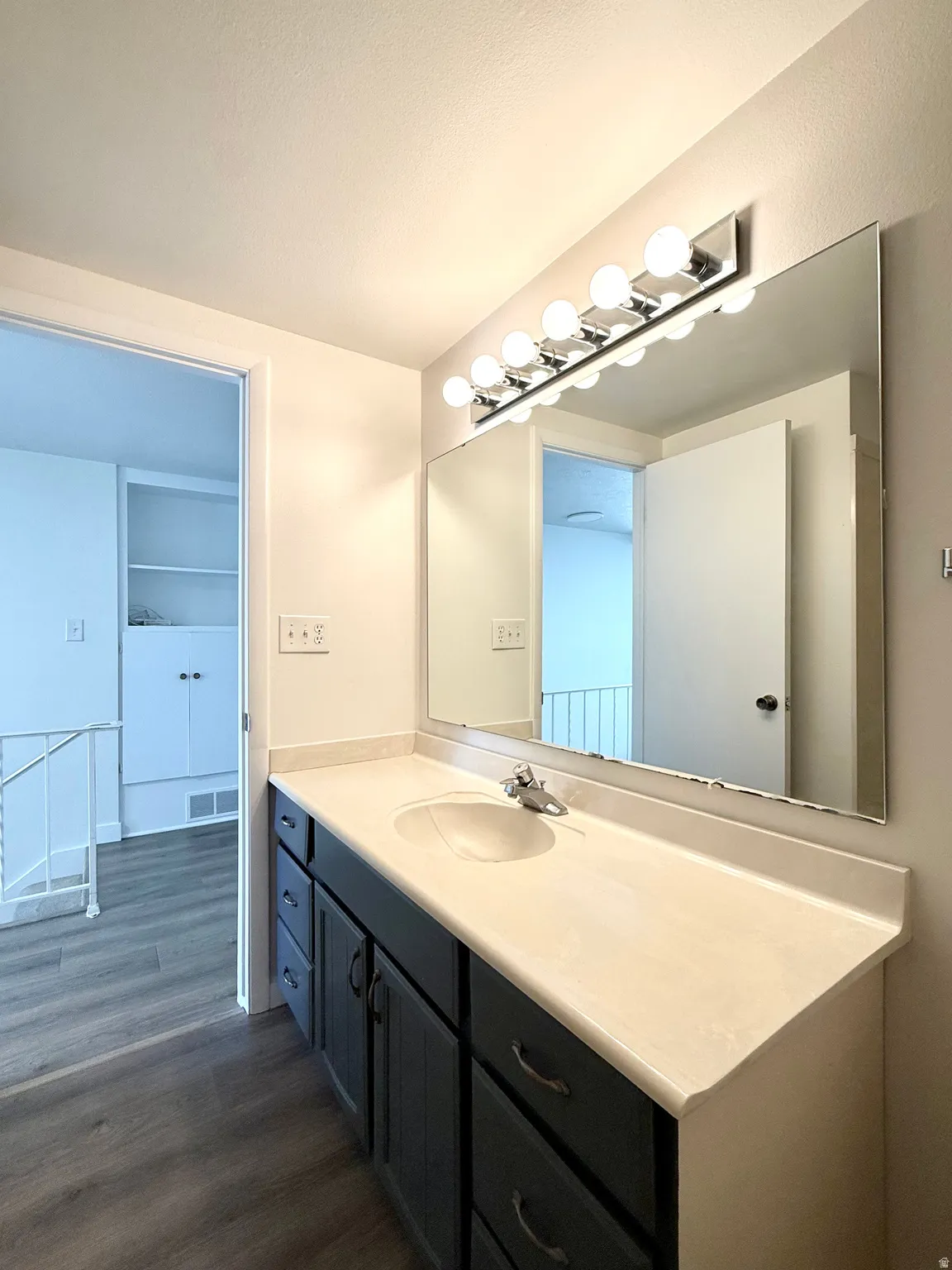 Extended vanity with integrated sink, chrome faucet, wall-mounted mirror, and multi-bulb vanity light fixture