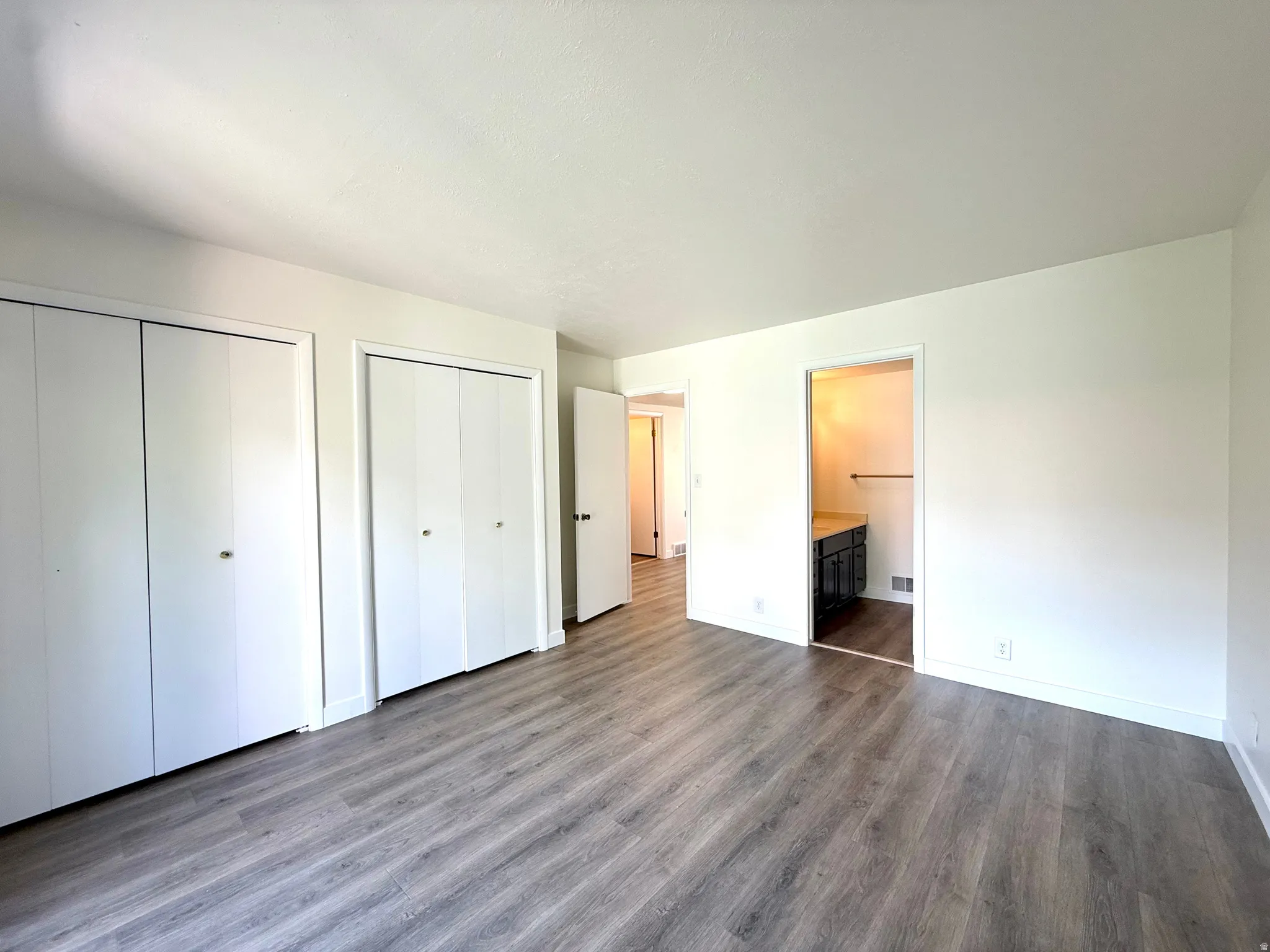 Wood-finish flooring throughout, bright white walls, and multiple bi-fold closet doors