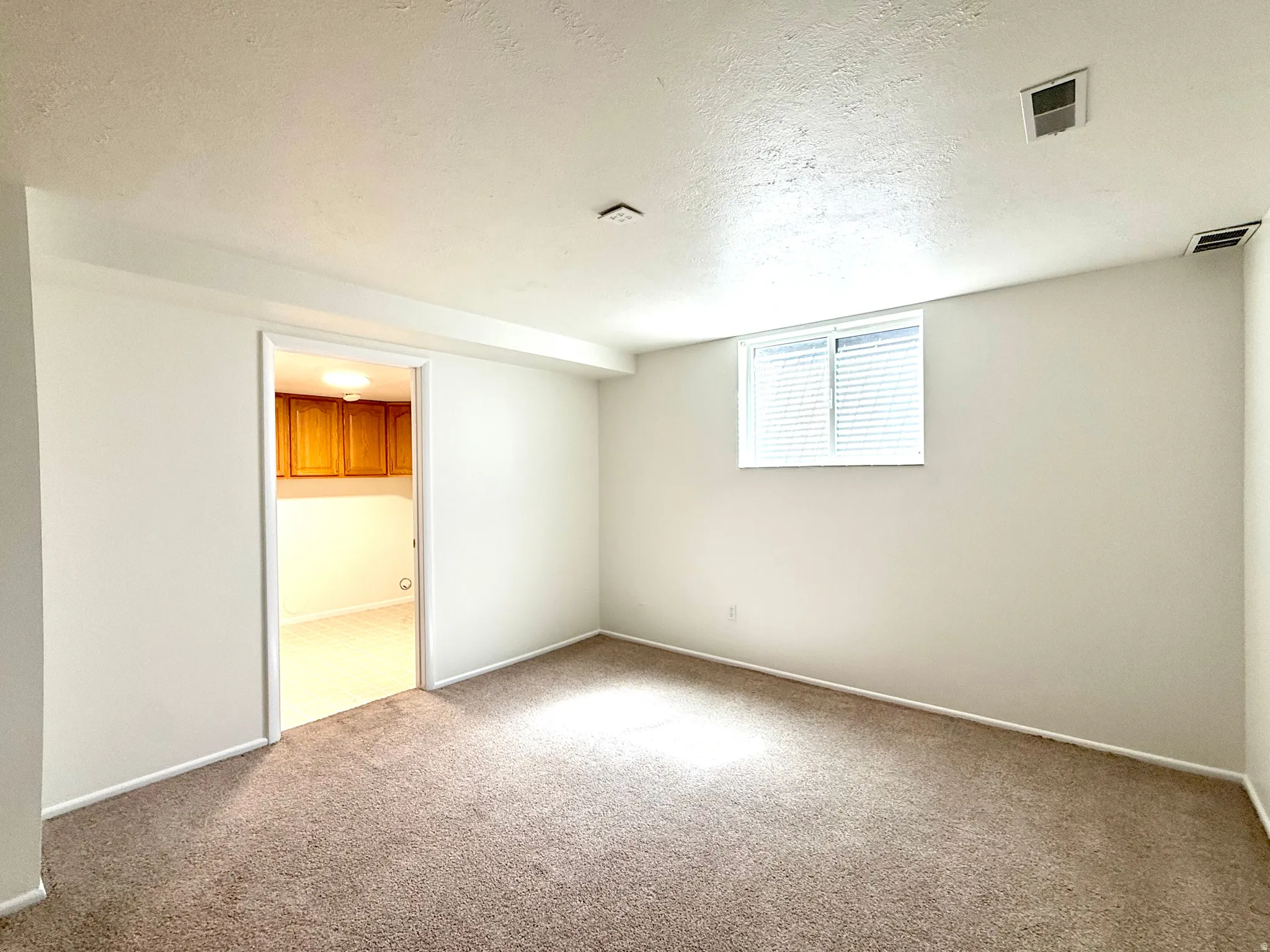 Carpeted flooring, white painted walls, window with blinds, recessed lighting, and a doorway leading to an additional space with wood-finish cabinetry