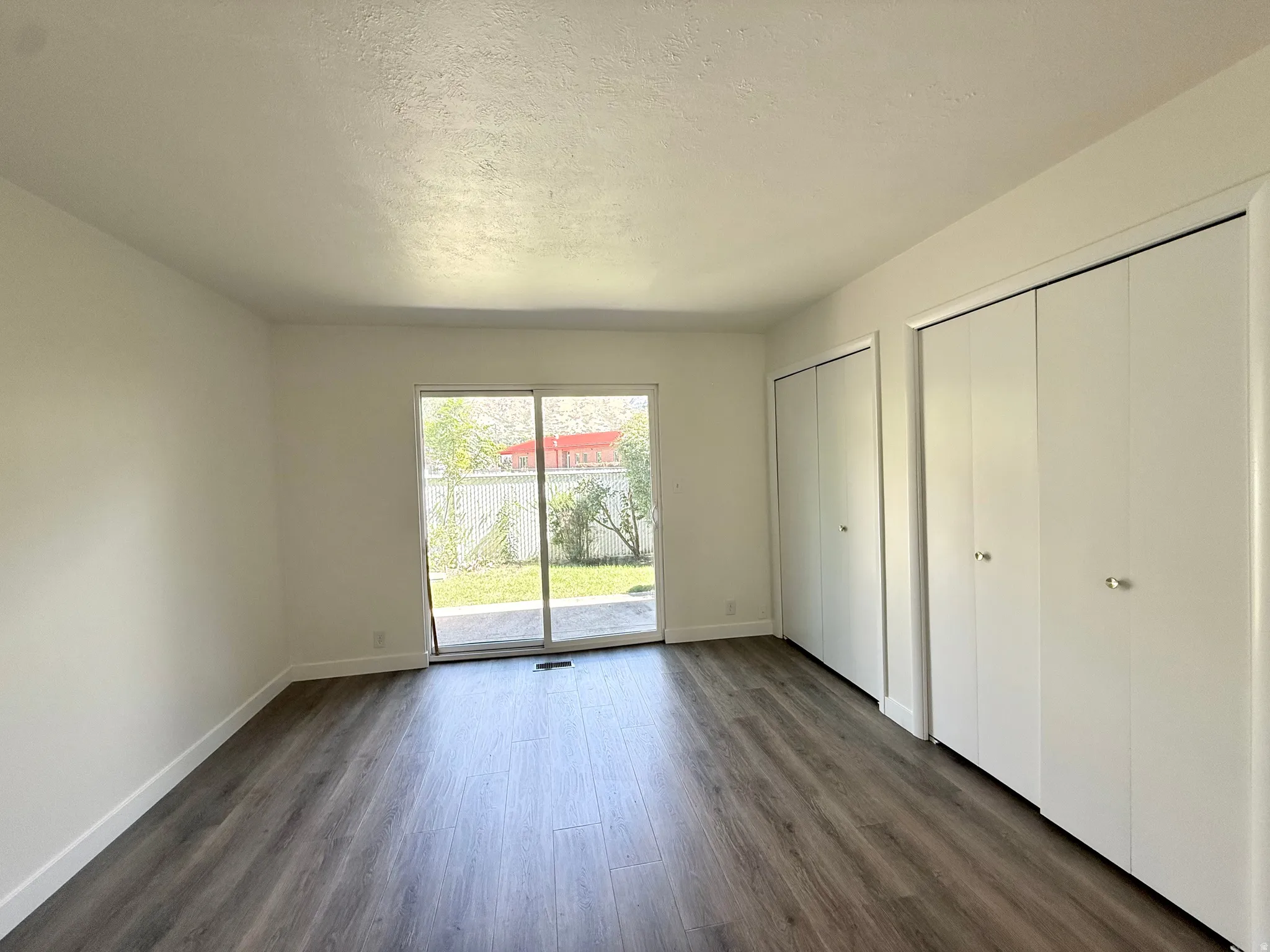 Wood-finish flooring, white walls, dual built-in closets, and a sliding glass door providing access to an exterior patio and lawn