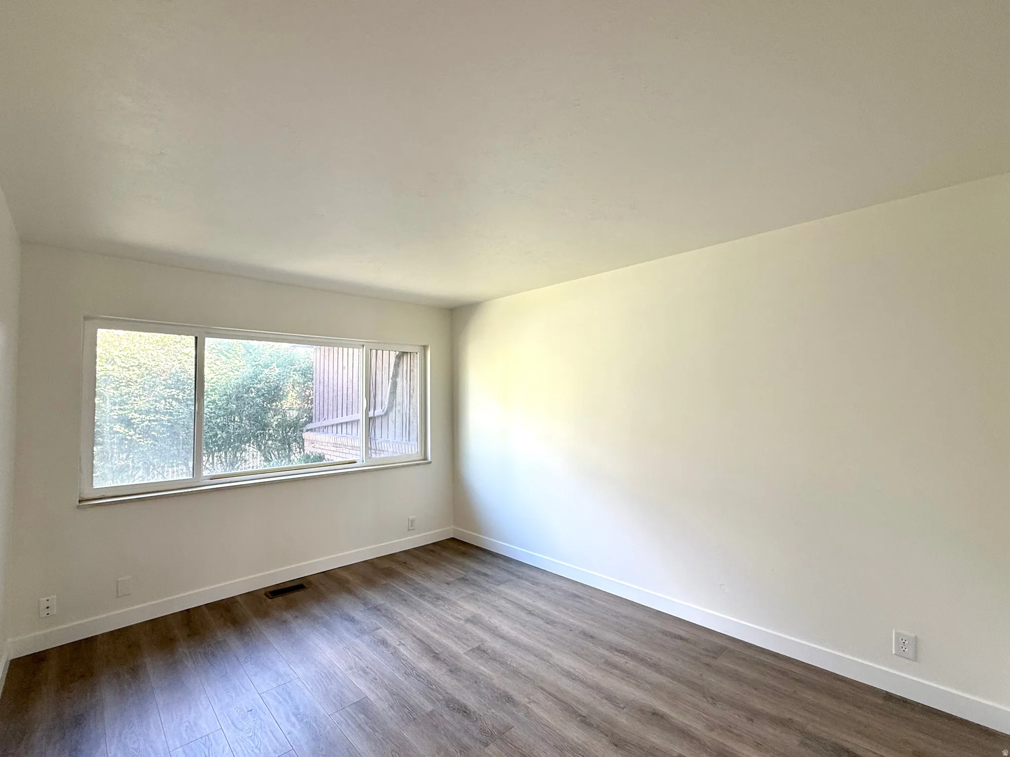 Large window with white frame, wood-finish flooring, and white walls