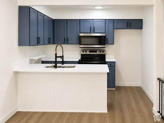 Kitchen featuring matte blue cabinetry, white countertops, stainless steel appliances, wood-finish flooring, and a high-arch kitchen faucet
