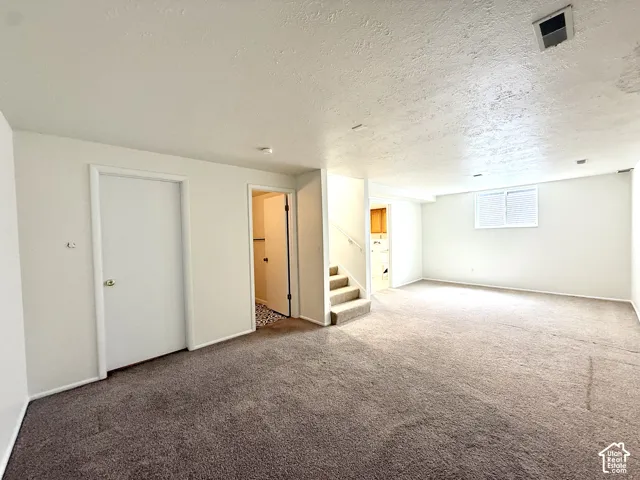 Carpeted room with white walls, a visible staircase, and an interior door