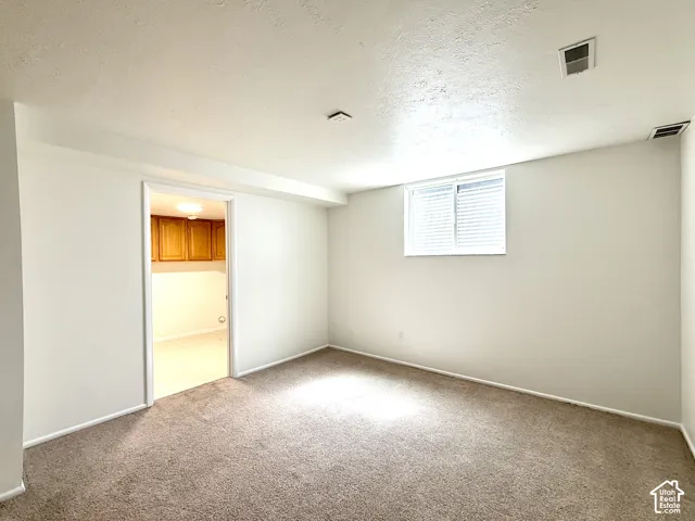 Carpeted flooring, white painted walls, window with blinds, recessed lighting, and a doorway leading to an additional space with wood-finish cabinetry