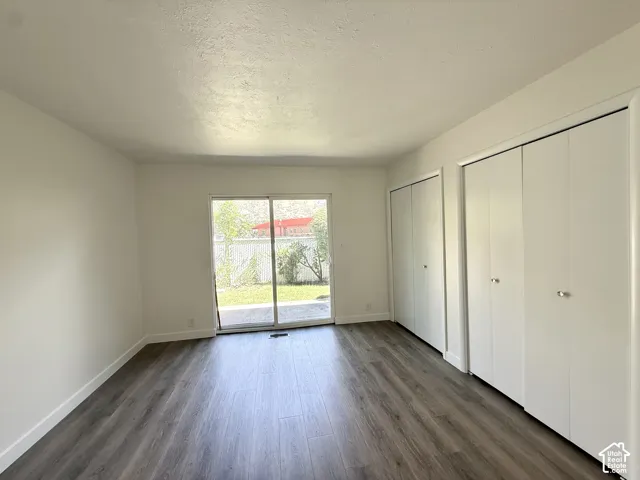 Wood-finish flooring, white walls, dual built-in closets, and a sliding glass door providing access to an exterior patio and lawn