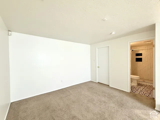 Carpeted room with recessed lighting and a white door, featuring an attached bathroom with patterned floor tiling, white subway tile shower, and built-in shower niches