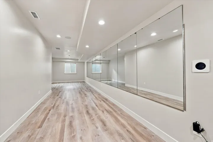Spacious room featuring wood-finish flooring, recessed lighting, a wall-mounted mirror installation, and a window.