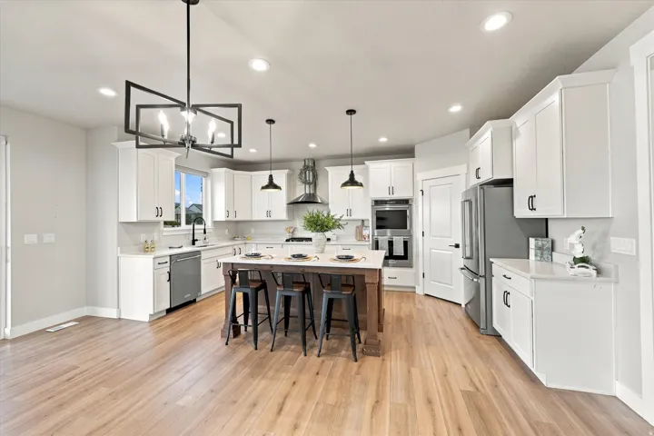 Spacious kitchen featuring light wood-finish flooring, white cabinetry, integrated stainless steel appliances, a center island with countertop seating, and recessed lighting.