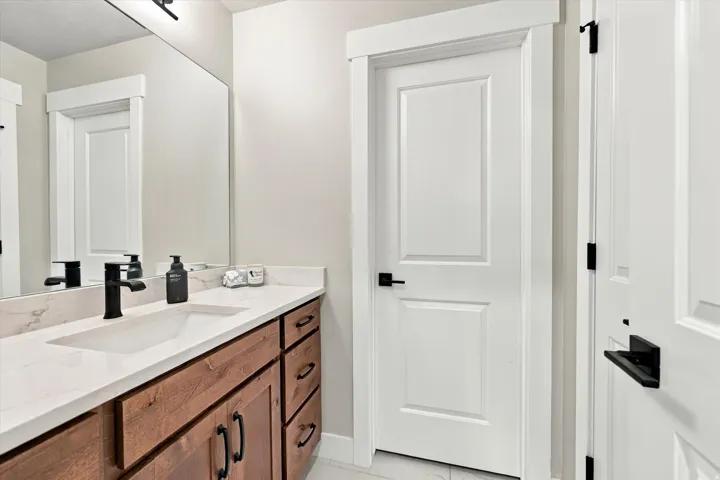 Wood-finish vanity with integrated sink, white countertop, matte black faucet, and rectangular mirror