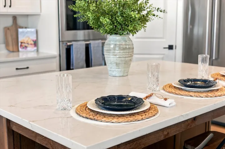 Kitchen island with a white quartz countertop, wood-finish base, stainless steel wall oven, and built-in stainless steel refrigerator.