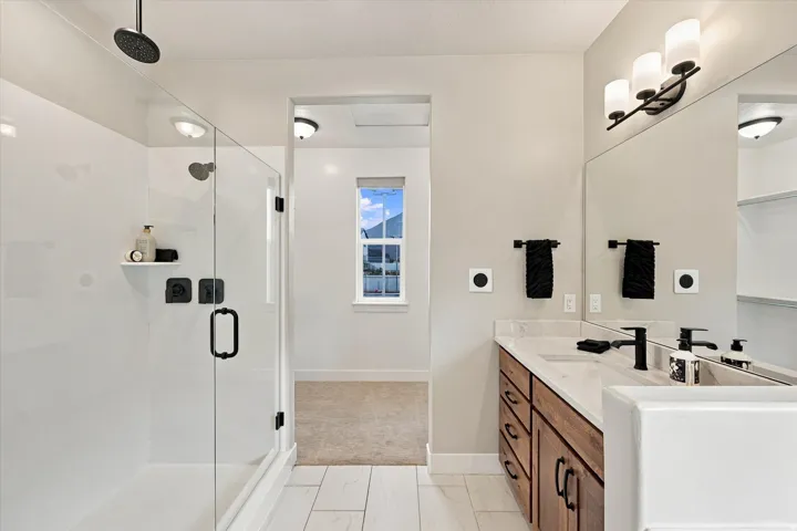 Contemporary bathroom featuring a glass-enclosed shower with matte black fixtures, a double vanity with wood-finish cabinetry, white countertop, and a large wall-mounted mirrors.