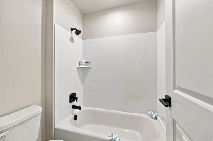 White bathtub with dark bronze fixtures, a wall-mounted showerhead, and a built-in corner shelf.