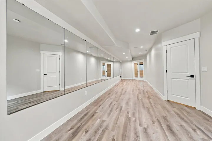 Work out gym with wood-finish flooring, recessed lighting, floor-to-ceiling mirrored wall, shaker-style doors with matte black hardware, and crisp white trim.