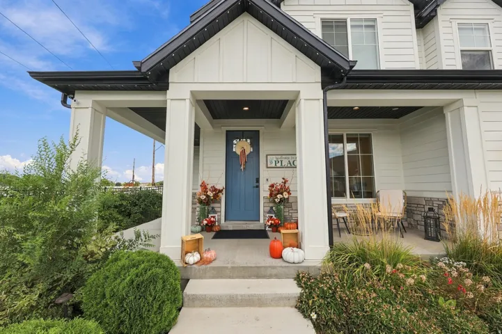 Front exterior featuring white siding, a contrasting dark roof, a covered porch with stone detailing, a blue entry door, and manicured landscaping