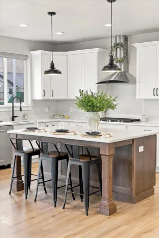 Wood-finish flooring, white cabinetry, stainless steel range hood, kitchen island with seating, and pendant lighting.