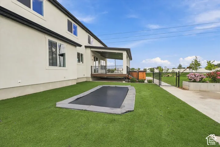 Expansive rear exterior featuring a covered deck, white stucco siding, and a lush green lawn.