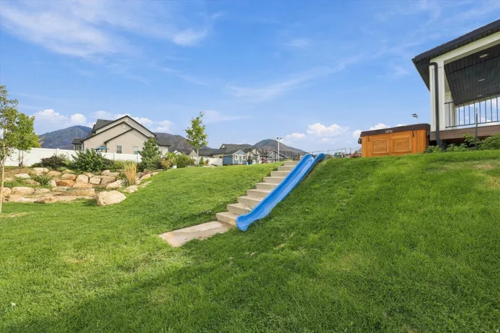 Expansive tiered lawn with natural rock landscaping, integrated concrete steps, a permanent slide feature and a fire pit for gatherings.