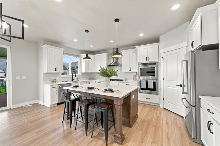 Light wood-finish flooring, white cabinetry, stainless steel appliances, central island with seating, and recessed lighting.