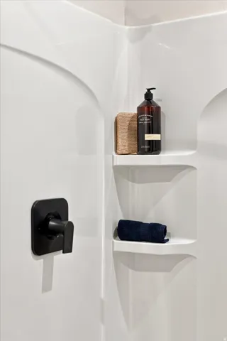 White shower surround with integrated shelving and matte black plumbing fixtures.