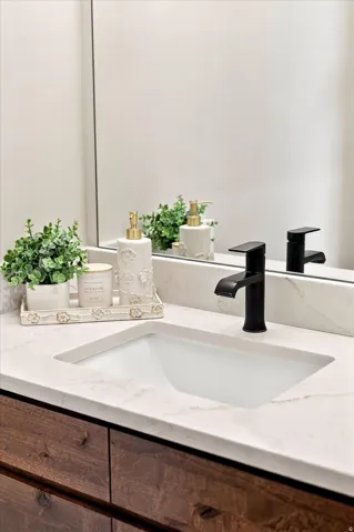 Half bathroom off of garage by kitchen. Undermount sink with a matte black single-handle faucet, set into a white countertop with a wood-finish vanity