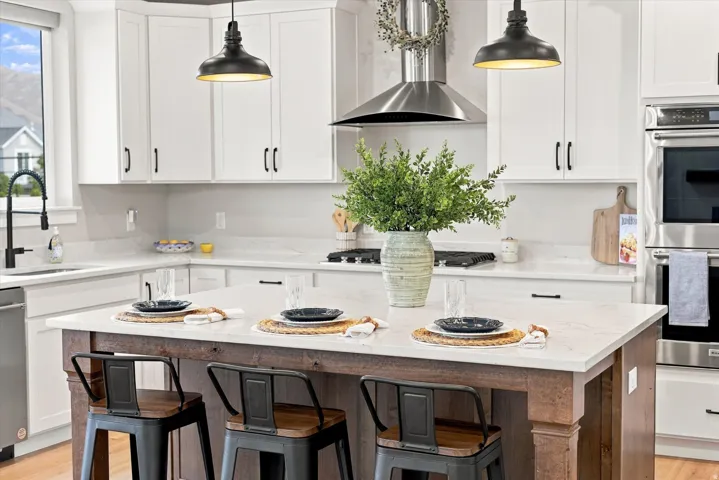 White shaker cabinetry, light-toned countertops, stainless steel appliances, a large wood-finish island, and pendant lighting.