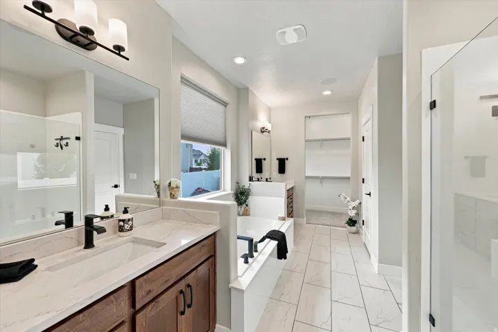 Owners bathroom with dual vanity with wood-finish cabinetry and light-toned countertops.
