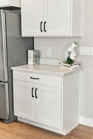 White shaker cabinetry with matte black hardware, light-toned countertop, and wood-finish flooring.