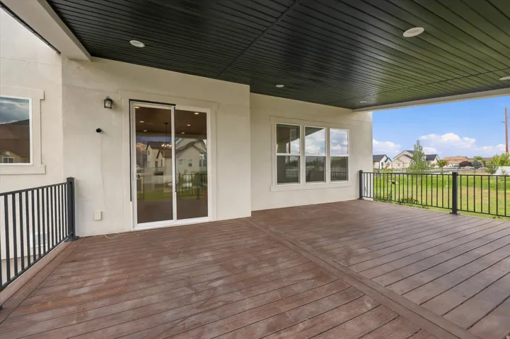 Covered outdoor deck with wood-finish flooring, recessed lighting, and black metal railings.