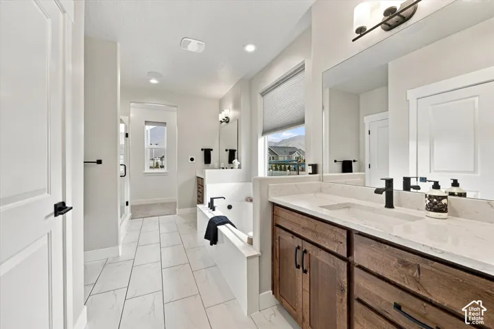Spacious owners  bathroom featuring white tiled flooring, a built-in bathtub, dual wood-finish vanity with stone countertops, and black fixtures.