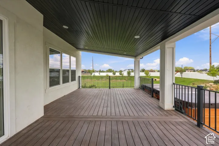 Expansive covered deck with wood-finish flooring, recessed lighting, white columns, and black metal railings.