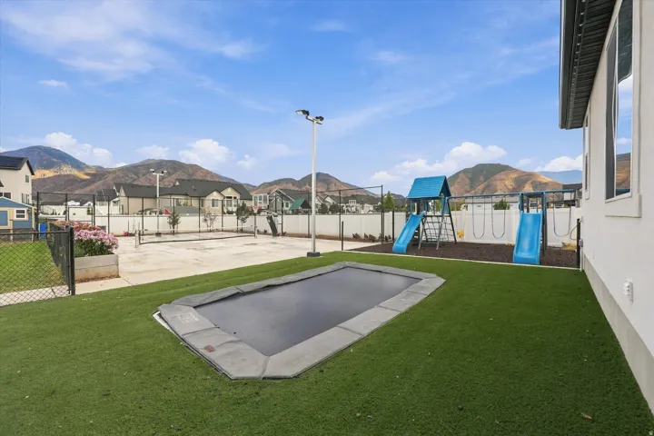 Expansive backyard featuring artificial turf, an in-ground trampoline, and a dedicated play structure with slides and swings.