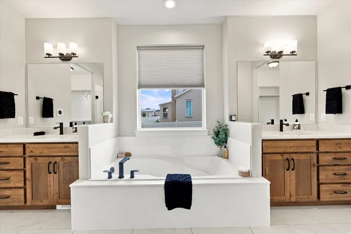 Dual vanities with wood-finish cabinetry white countertops and a soaker tub.