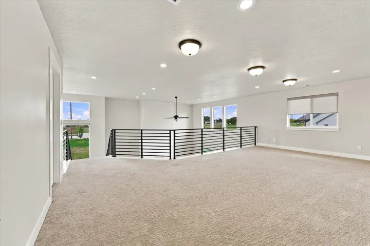 Carpeted loft area featuring a contemporary horizontal railing, multiple windows, and recessed lighting with additional flush-mount fixtures.