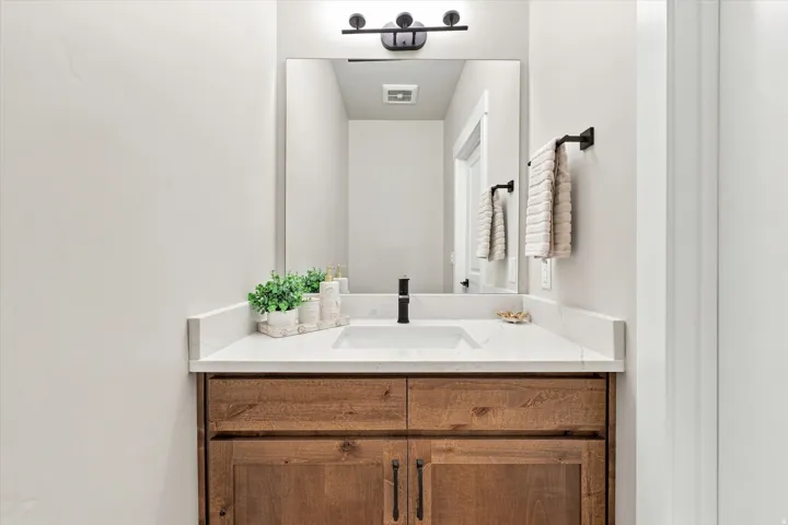 Half bathroom off kitchen. Wood-finish vanity with an integrated rectangular sink, stone countertop, and matte black faucet