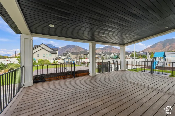 Covered deck featuring wood-finish flooring, recessed lighting, white columns, and black metal railings.