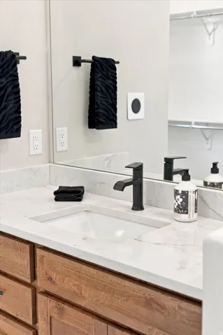 Wood-finish vanity with white undermount sink, solid surface countertop, and matte black faucet.