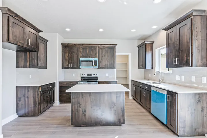 Kitchen featuring wood-finish cabinetry, light-toned countertops, a central island, and stainless steel appliances