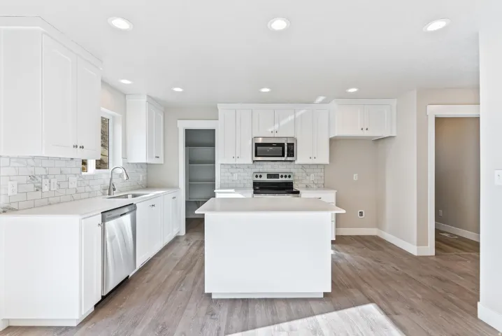 White cabinetry, stainless steel appliances, wood-finish flooring, recessed lighting, and a kitchen island