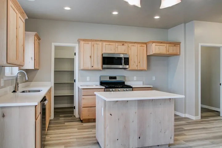 Kitchen featuring light wood cabinetry, white countertops, stainless steel appliances, a center island, and wood-finish flooring