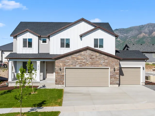Two-story residence featuring a stone and siding exterior, an attached two-car garage, an additional attached single-car garage, a concrete driveway, and a front lawn with young trees