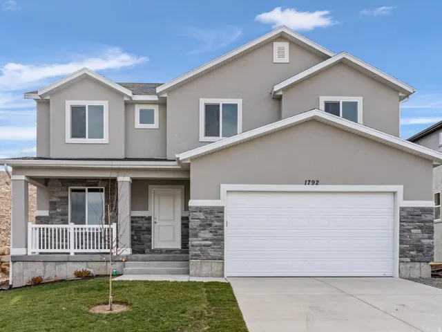 Two-story residence featuring a covered entry porch, attached two-car garage, and a combination of stucco and stone veneer exterior finishes