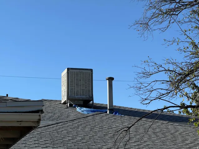 Asphalt shingle roof with a central evaporative cooler and a metal vent pipe