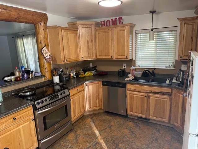 Wood-finish cabinetry, dark countertops, stainless steel appliances, and a log-framed pass-through window