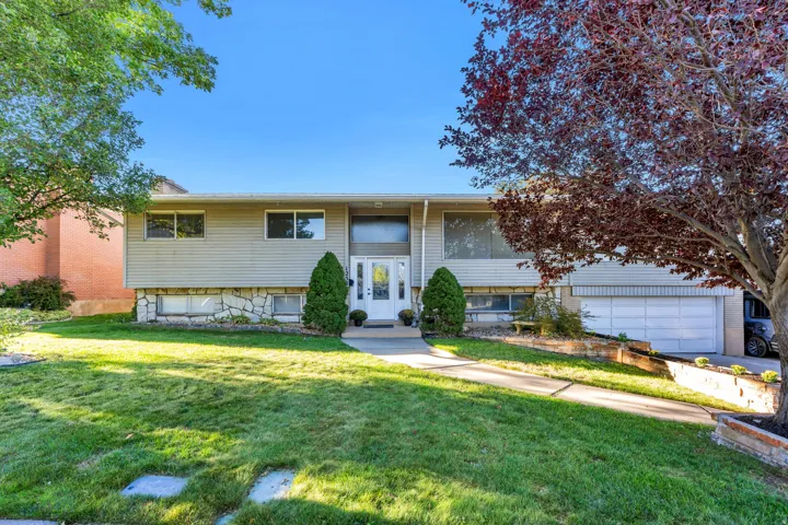 Split-level residence featuring a two-car garage, stone facade accents, and a mature front yard with established trees