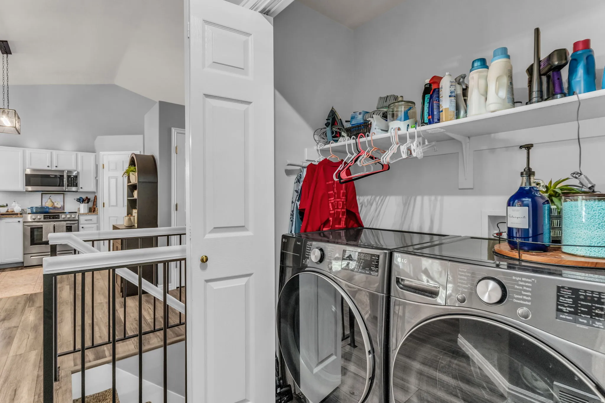 Dedicated laundry area with built-in shelving, wood-finish flooring, and a railing with metal spindles