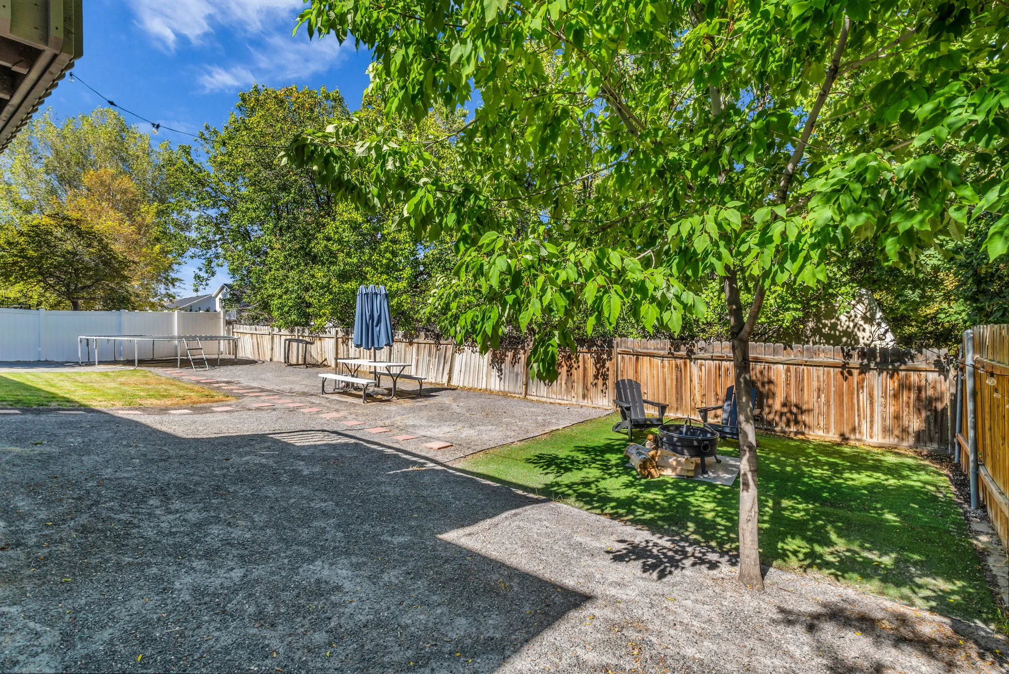 Expansive outdoor space featuring gravel and artificial turf areas, mature trees, and a wooden fence