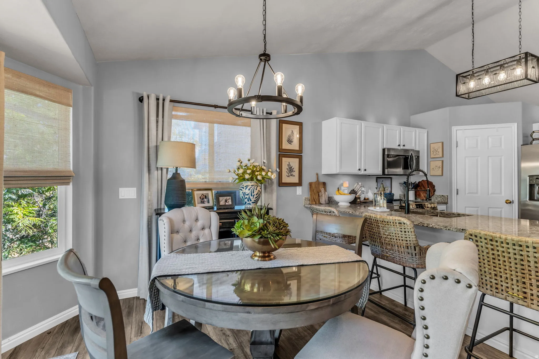 Kitchen and dining area featuring vaulted ceilings, wood-finish flooring, white cabinetry, a kitchen island with seating, and a modern chandelier