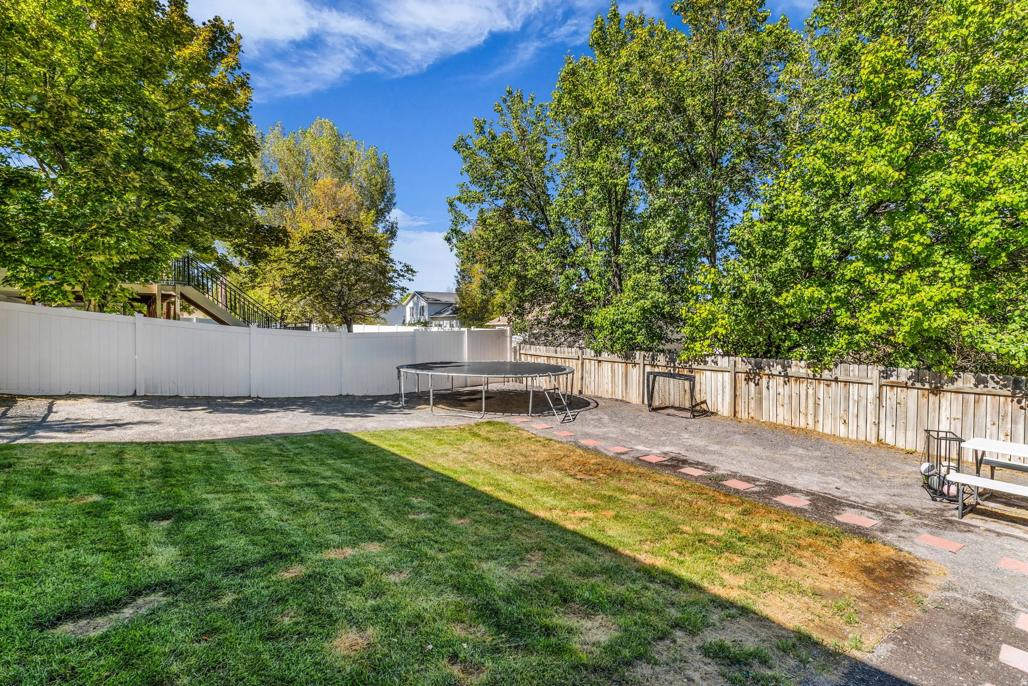 Expansive backyard featuring a partial manicured lawn, a gravel patio area, and a white privacy fence
